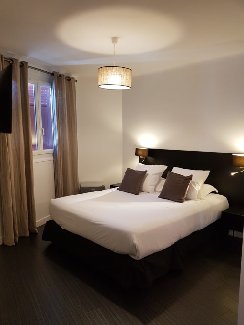 Modern bedroom at Hotel Au Bon Coin in Biarritz with black bed frame, white linens, pendant light, and elegant décor