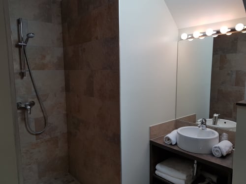 Modern bathroom at Hotel Au Bon Coin in Biarritz with round sink, large mirror with vanity lights, and walk-in shower with