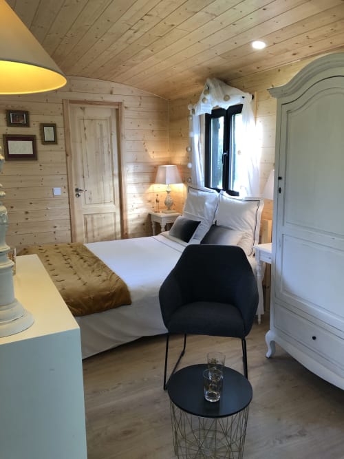 Chambre moderne à La roulotte du Moulin De La Chevrière à Saché, avec murs en bois, lit blanc, chaise noire et grandes fenêtres