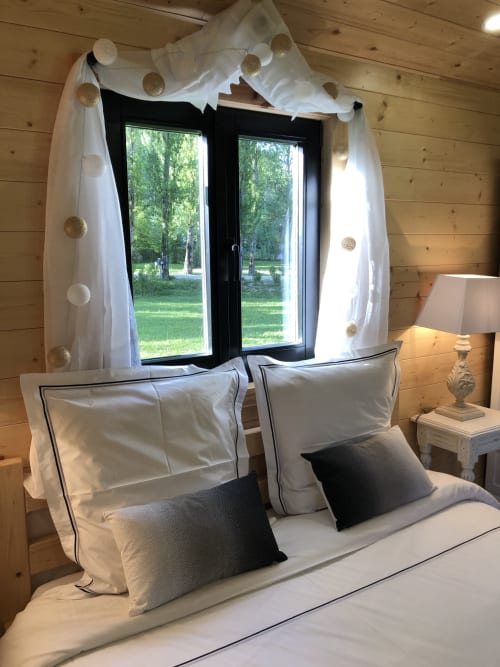 Chambre élégante au Moulin De La Chevrière avec literie blanche, oreillers noirs, rideaux drapés et vue sur la rivière forestière