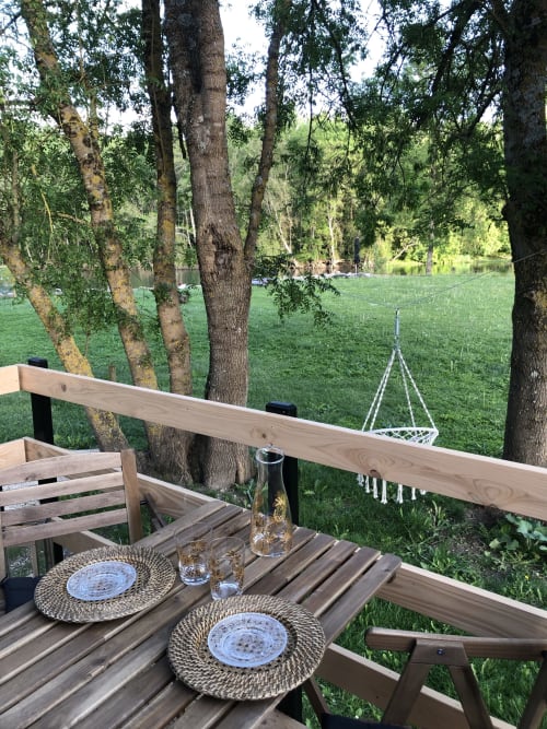 Coin repas en plein air sur terrasse en bois au Moulin De La Chevrière avec vue sur la rivière, couverts et jardins verdoyants