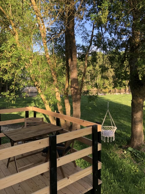 Terrasse en bois avec chaise suspendue blanche surplombant la pelouse verdoyante et la rivière au Moulin De La Chevrière, Saché
