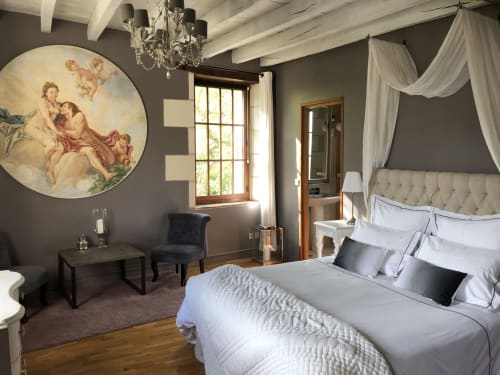 Chambre élégante au Moulin De La Chevrière avec lit à baldaquin, lustre orné et tableaux classiques surplombant la rivière