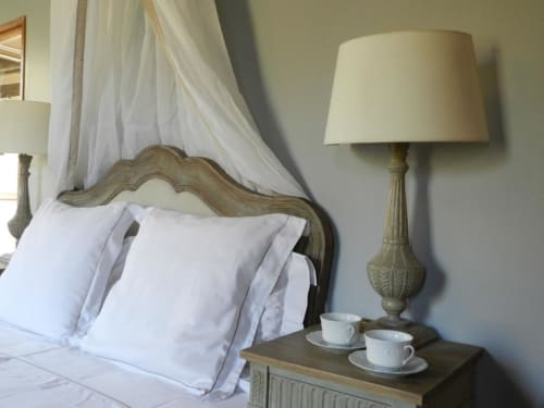 Chambre élégante au Moulin De La Chevrière avec tête de lit sculptée, draps blancs et lampe de chevet avec service à thé