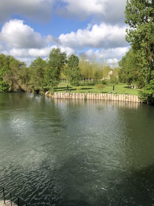 Vue paisible de la rivière au Moulin De La Chevrière à Saché avec un quai en bois, végétation luxuriante et ciel bleu