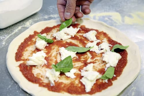 Main garnissant une pizza Margherita fraîche avec du basilic à l'Hôtel La Trelade, St Martins