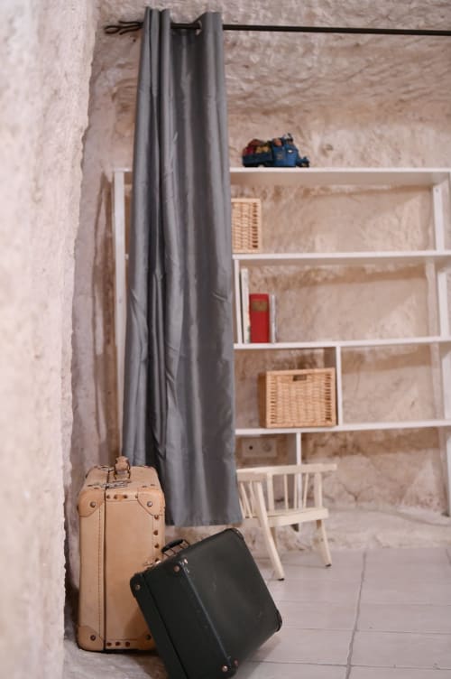 Valises vintage beige et noires dans une chambre de gîte rustique aux rideaux gris et étagères blanches aux Gîtes des Châteaux