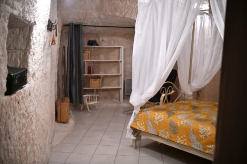Chambre rustique avec lit à baldaquin blanc, couette motifs moutarde, murs en pierre et coin détente aux Gîtes des