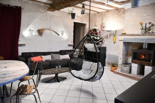 Salon rustique avec fauteuil suspendu noir, cheminée et coin salon aux gîtes des châteaux