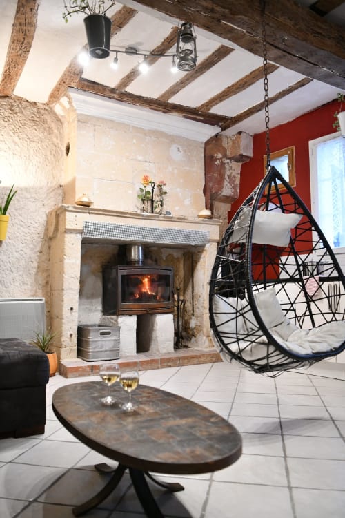 Salon rustique avec cheminée, fauteuil suspendu, poutres apparentes et mur rouge aux gîtes des châteaux