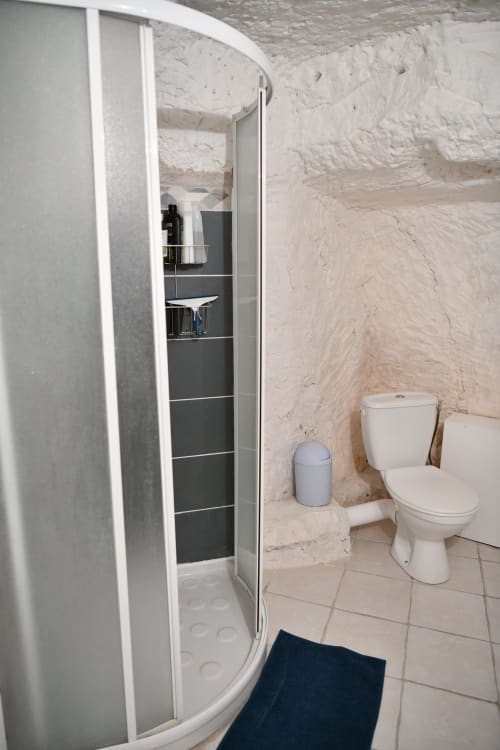Salle de bain compacte au gîte Le troglo du boy'fini aux Gîtes des châteaux avec douche, toilettes et murs en pierre blanche