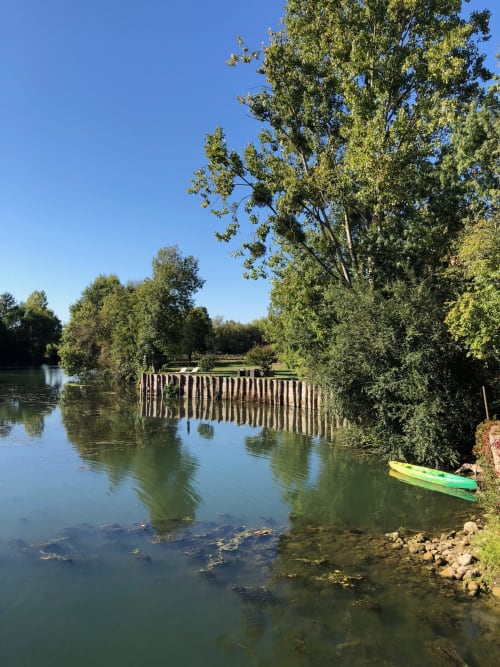 Vue paisible de la rivière au Moulin De La Chevrière à Saché avec kayak, pont en bois et arbres verdoyants sous ciel bleu