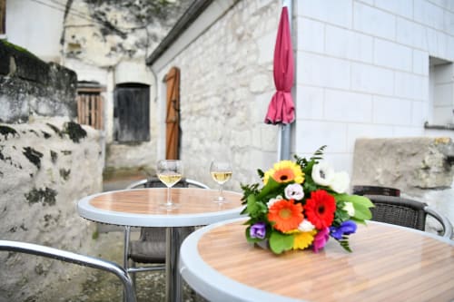 Patio de charme aux gîtes des châteaux avec fleurs colorées, verres de vin et parasol rose