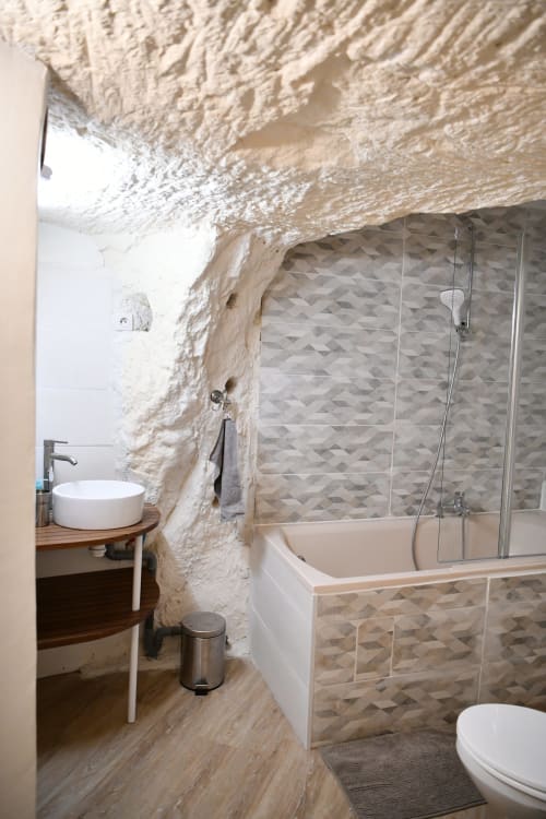 Salle de bain troglodytique à Vallières-les-Grandes avec murs de pierre, équipements modernes, baignoire, douche et mobilier arrondi