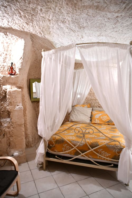 Chambre troglodytique avec lit à baldaquin et literie orange aux Gîtes des Châteaux, Vallières-les-Grandes