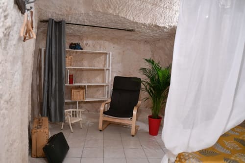 Intérieur de gîte troglodytique aux Châteaux : fauteuil bois, étagères, plante en pot et murs en pierre