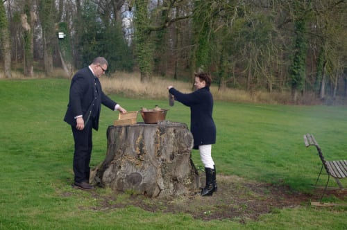 Couple planting a tree at Château d'Hassonville BnB in Marche-en-Famenne, Belgium, with woodland backdrop.