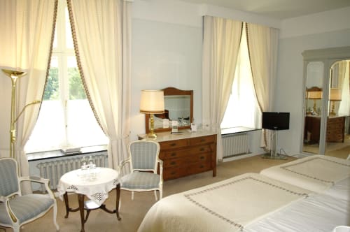 Elegant bedroom suite at Château d'Hassonville B&B in Marche-en-Famenne, Belgium, with cream drapes, period furniture and