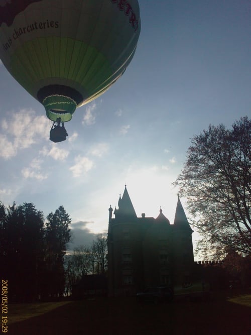 Green hot air balloon floating above Château d'Hassonville castle in Marche-en-Famenne, Belgium