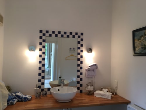Modern bathroom sink with white bowl basin, black and white checkered mirror frame, and wall-mounted lighting at La
