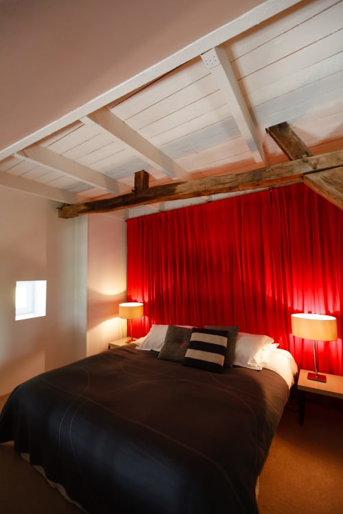 Modern bedroom at Moulin Renaudiots in Autun with red curtains, exposed wooden beam, and contemporary white ceiling