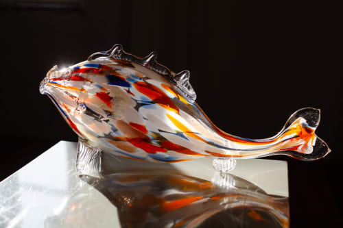 Colorful glass fish sculpture with red and blue striped design on white surface at Moulin Renaudiots hotel in Autun