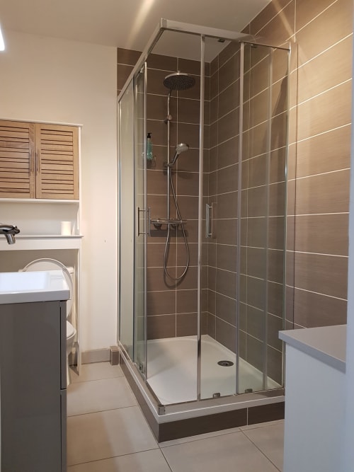 Salle de bain moderne de l'hôtel Les Cabines avec douche vitrée, murs en carrelage foncé et meuble-lavabo sombre