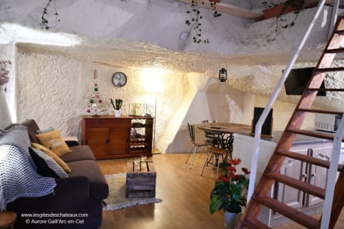 Intérieur cosy du gîte des châteaux avec murs en pierre, mobilier en bois, coin salon et escalier en spirale