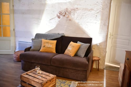 Espace détente douillet au gîte Le troglo'riel des Gîtes des Châteaux avec canapé marron, coussins jaunes et table en bois