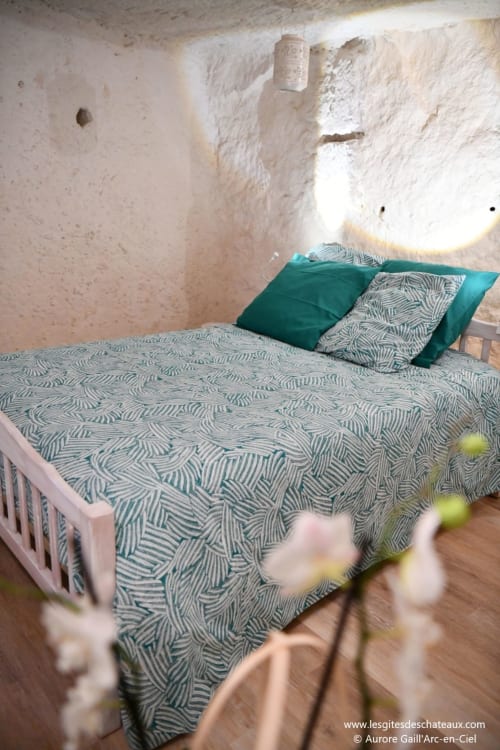 Chambre cosy aux gîtes des châteaux avec literie à motifs, oreillers turquoise, murs chaulés et lumière naturelle