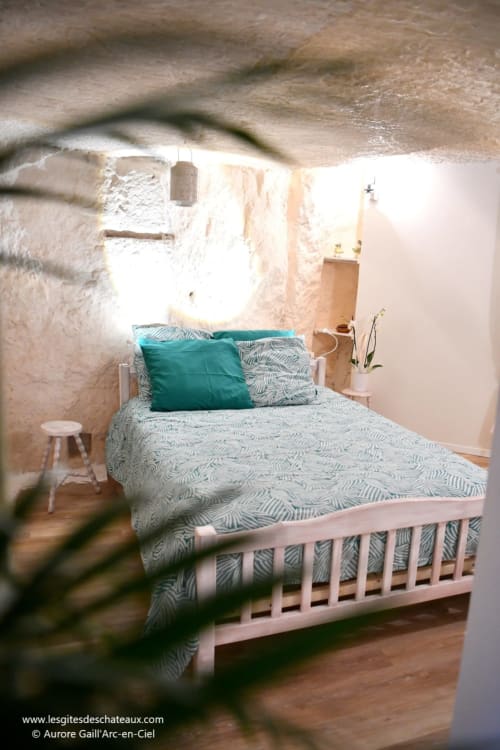 Chambre cosy du gîte Le troglo'riel aux Gîtes des Châteaux : murs en pierre blanche, literie à motifs et touches de vert
