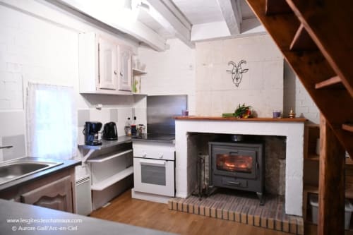 Cuisine de gîte avec poêle à bois, meubles blancs et appareils modernes aux Gîtes des Châteaux