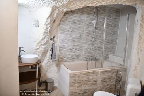 Salle de bain moderne avec baignoire, paroi vitrée et murs en pierre aux gîtes des châteaux à Vallières-les-Grandes, France