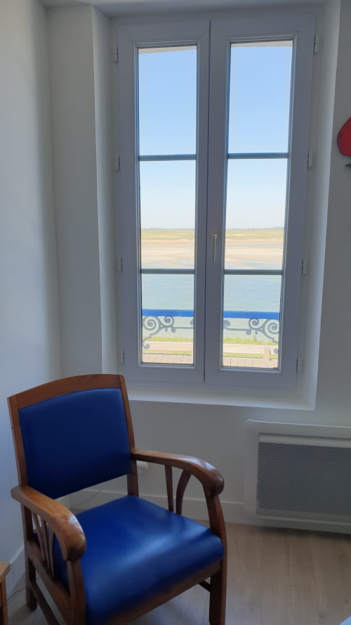 Chaise en bois rembourrée de bleu face aux portes-fenêtres avec vue sur la mer à la maison d'hôtes Vue D'ici, Saint-Valéry-sur-Somme