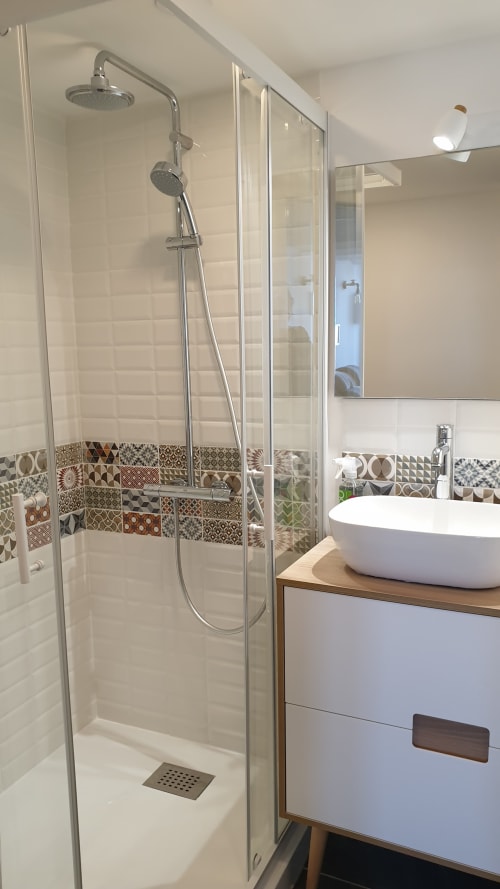 Salle de bain moderne avec douche vitrée, vasque blanche et carrelage décoratif à la maison d'hôtes Vue D'ici à Saint