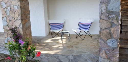 Zwei gestreifte Strandstühle und kleiner Tisch auf der Steinterrasse des Ty Pals B&B in Pals, Spanien, mit blühenden Pflanzen