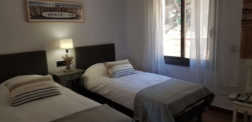 Twin bedroom at Ty Pals B&B in Pals with striped pillows, bedside lamp, and garden view through curtained windows