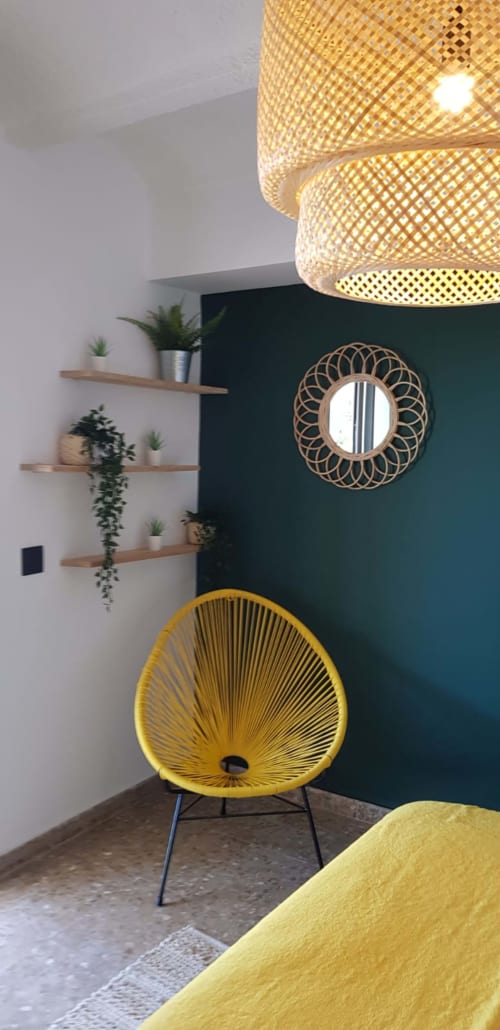 Ty Pals bedroom corner with yellow chair, woven pendant lamp, potted plants on wooden shelves, and teal accent wall