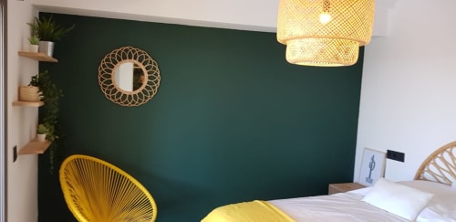 Modern bedroom at Ty Pals B&B in Pals with forest green accent wall, yellow chairs, woven mirror, and wooden pendant light