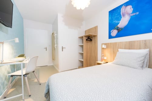 Chambre moderne à Un Air De Famille à Vittel avec lit, bureau, œuvre d'art bleue, rangements en bois et télévision