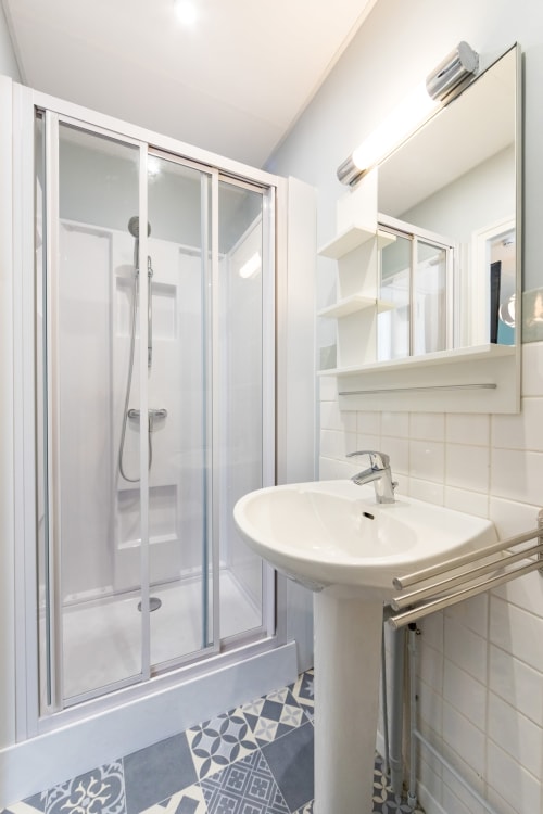 Salle de bains moderne et partagée avec carrelage blanc, lavabo sur colonne, miroir armoire et douche vitrée à Un Air De Famille