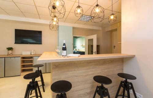 Espace bar moderne avec comptoir en bois, tabourets noirs et luminaires géométriques suspendus à Un Air De Famille B&B à Vittel, France