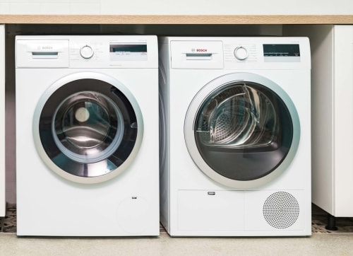 Deux machines à laver Bosch blanches et un sèche-linge dans la buanderie du gîte Un Air De Famille, Vittel France