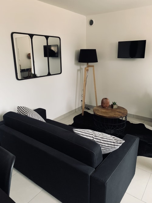 Moderne woonkamer van het huisje La Maison D'ambrine met zwarte bank, wandmonteerde TV, houten bijzettafel en modern interieur