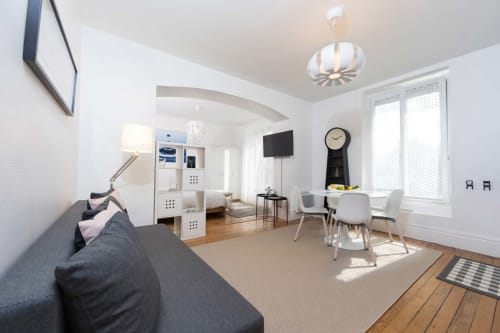 Studio moderne à Un Air De Famille à Vittel avec canapé gris, meuble de rangement blanc, coin repas et grandes fenêtres