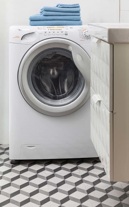 Lave-linge blanc frontal avec serviettes bleues empilées dessus dans un studio à Un Air De Famille, Vittel