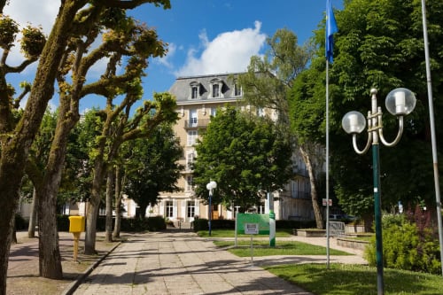 Cour ombragée de l'établissement Un Air De Famille à Vittel, avec bâtisse historique et lampadaire