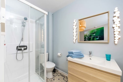 Salle de bain moderne du studio Un Air De Famille à Vittel, avec douche, vasque, serviettes bleues et éclairage décoratif