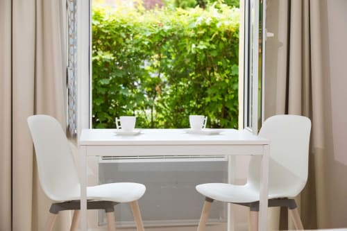 Studio moderne Un Air De Famille à Vittel avec table à manger blanche, chaises et vue sur le jardin par grande fenêtre