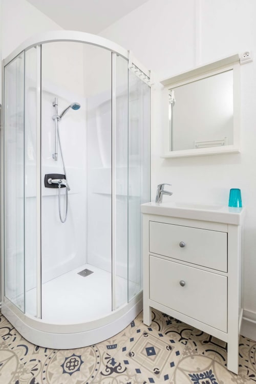 Salle de bain moderne avec douche en verre courbe, vanité blanche et sol à motifs à Un Air De Famille Vittel BnB